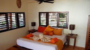 A neatly made bed with orange and white bedding, two bedside lamps, and a ceiling fan. - Hotel Sol Caribe (Punta Allen)