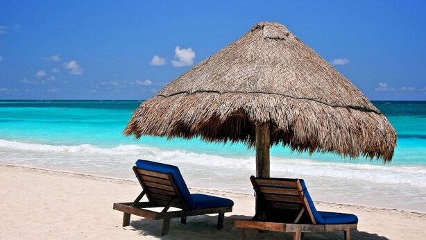 A beach with two wooden lounge chairs under a thatched umbrella, overlooking turquoise waters. - Hotel Sol Caribe (Punta Allen)