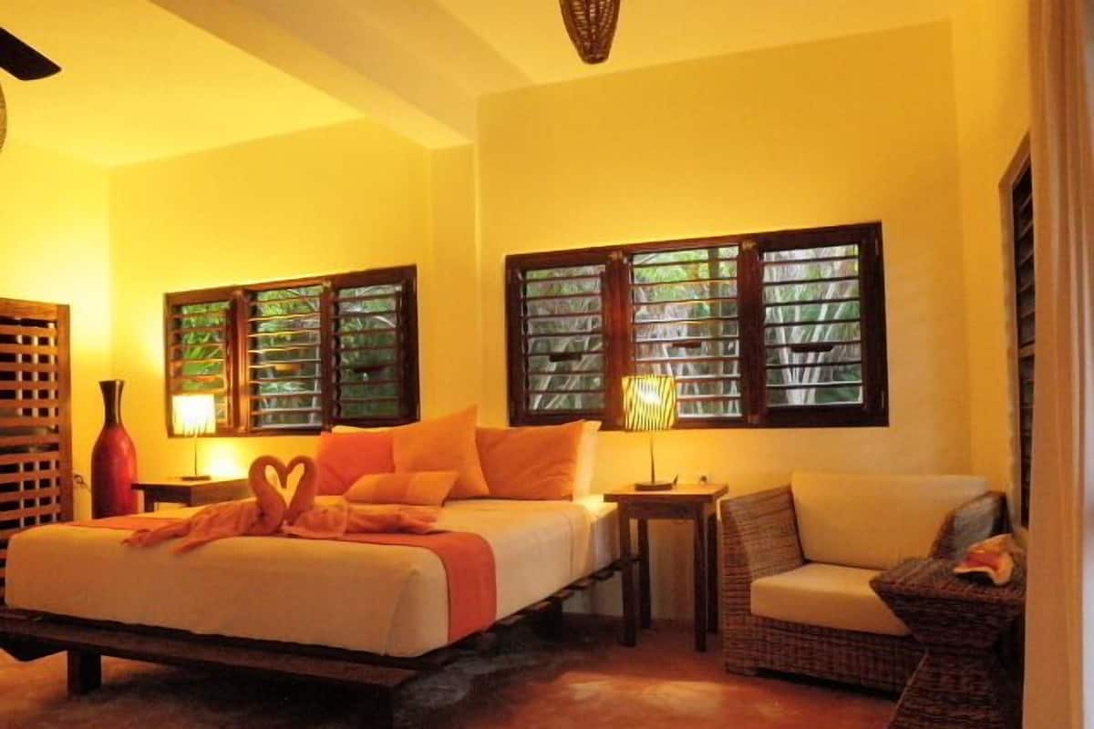 A bedroom with a bed, two nightstands, a chair, and a window with shutters.