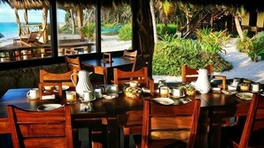 A dining area with wooden tables and chairs, a white pitcher, and various dishes. - Hotel Sol Caribe (Punta Allen)