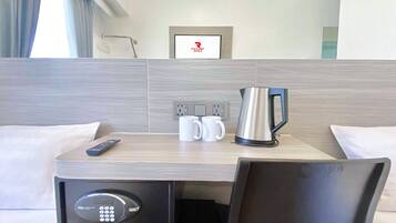 A hotel room with a bed, a desk with a coffee maker, a remote control, and a TV.