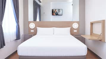 A modern hotel room with a large bed, a headboard with integrated lighting, a bedside table, and a wall-mounted shelf.