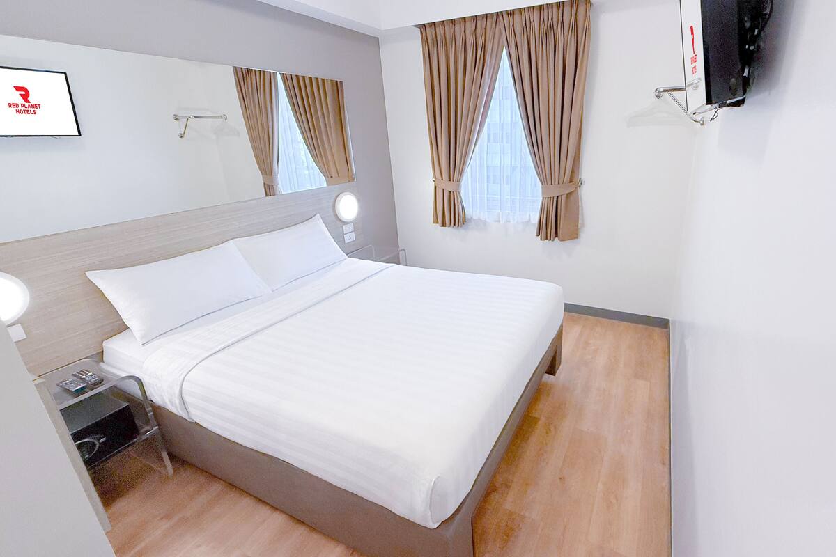 A hotel room with a large bed, bedside tables, a TV mounted on the wall, and curtains on the windows.