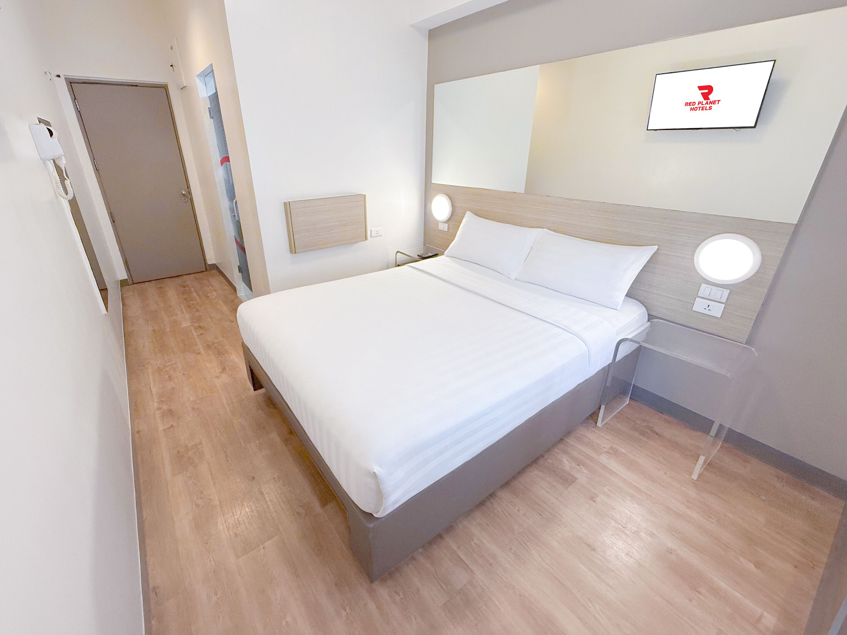 Une chambre d’hôtel moderne avec un lit, un téléviseur fixé au mur et un plancher en bois.
