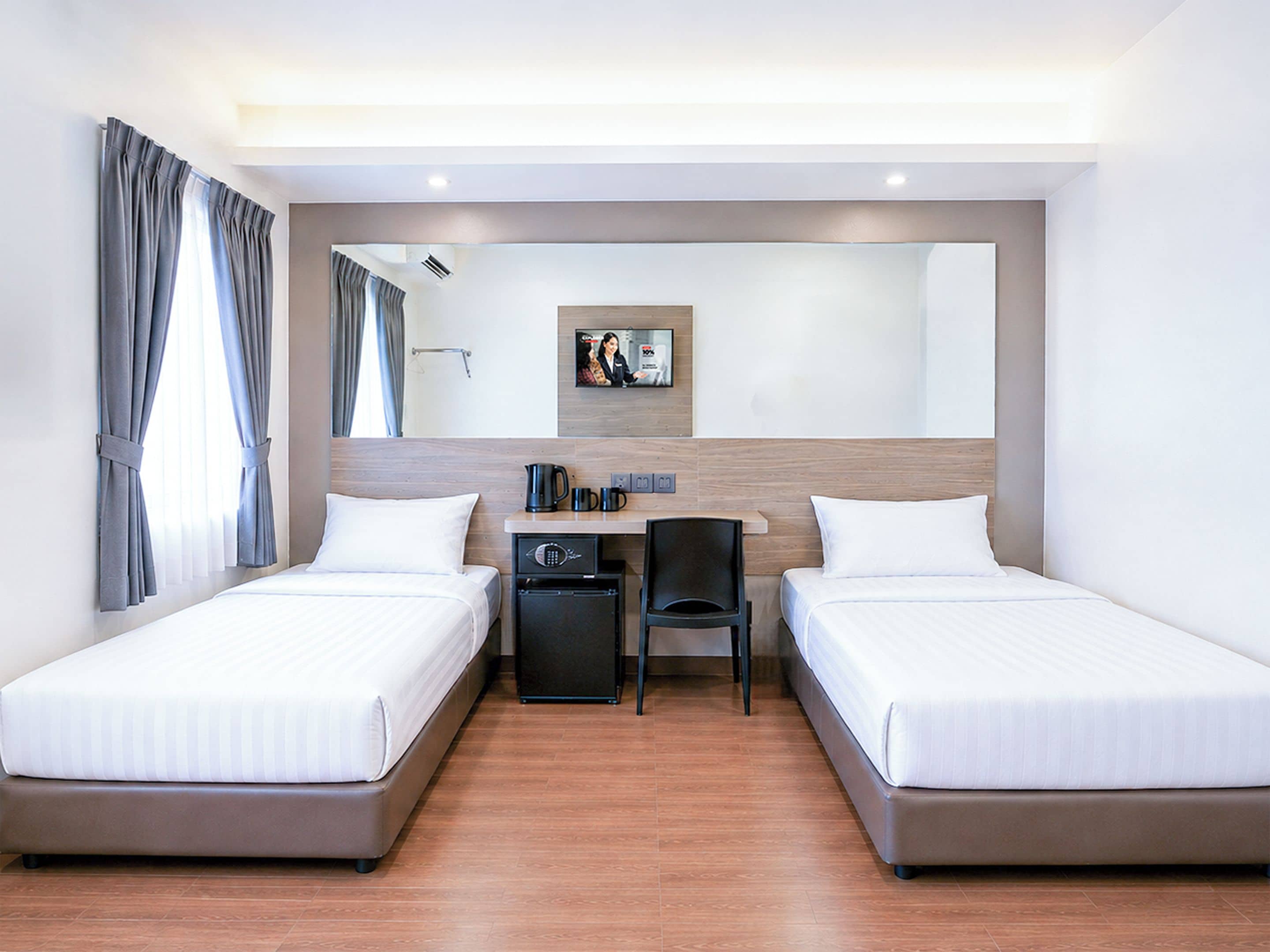 A hotel room with two beds, a desk, a chair, a coffee maker, and a small refrigerator.