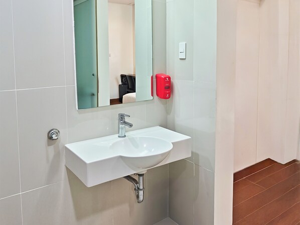 Un baño con un lavamanos blanco, un espejo y un dispensador de jabón rojo.