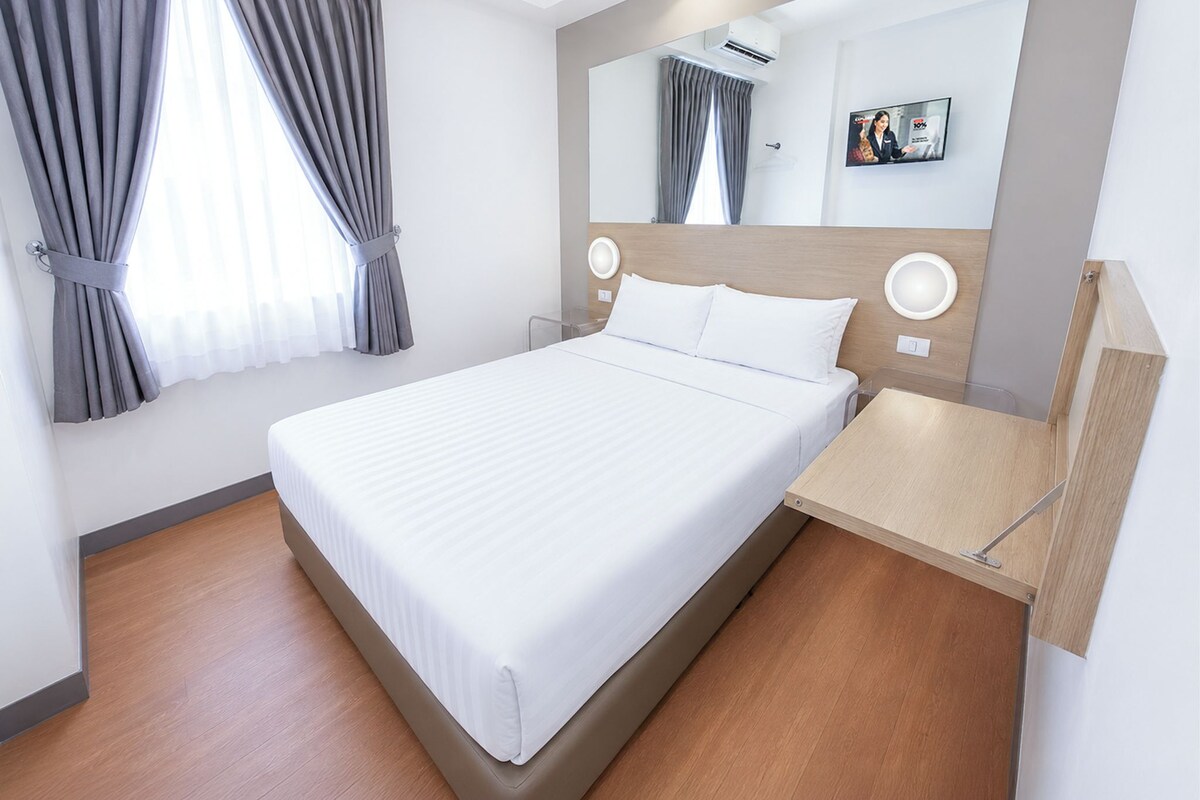 A hotel room with a large bed, a bedside table, a mirror, and a window with curtains.