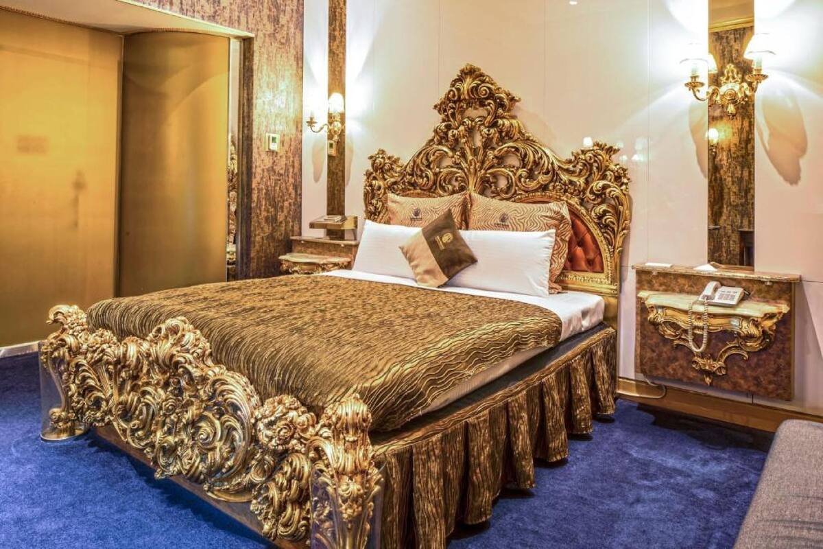 A luxurious bedroom with an ornate bed, a nightstand with a telephone, and a wall-mounted lamp.