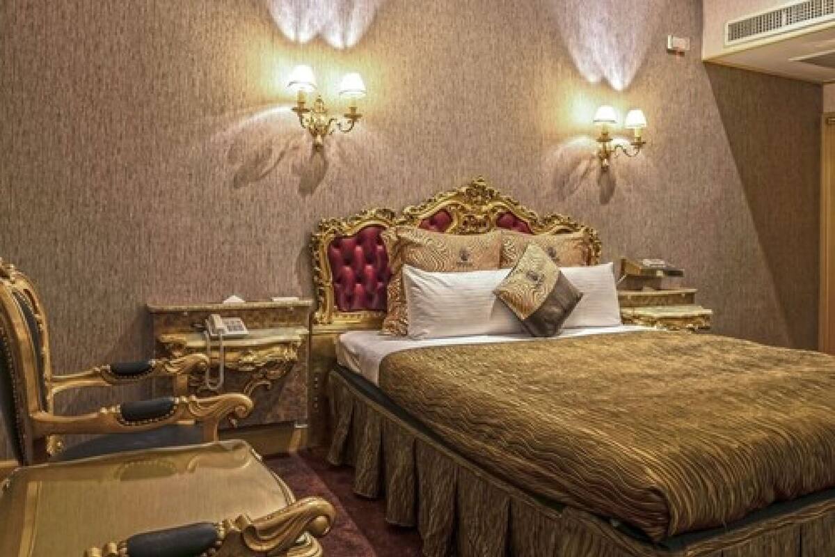 A luxurious bedroom with a large bed, ornate headboard, and a nightstand with a telephone.