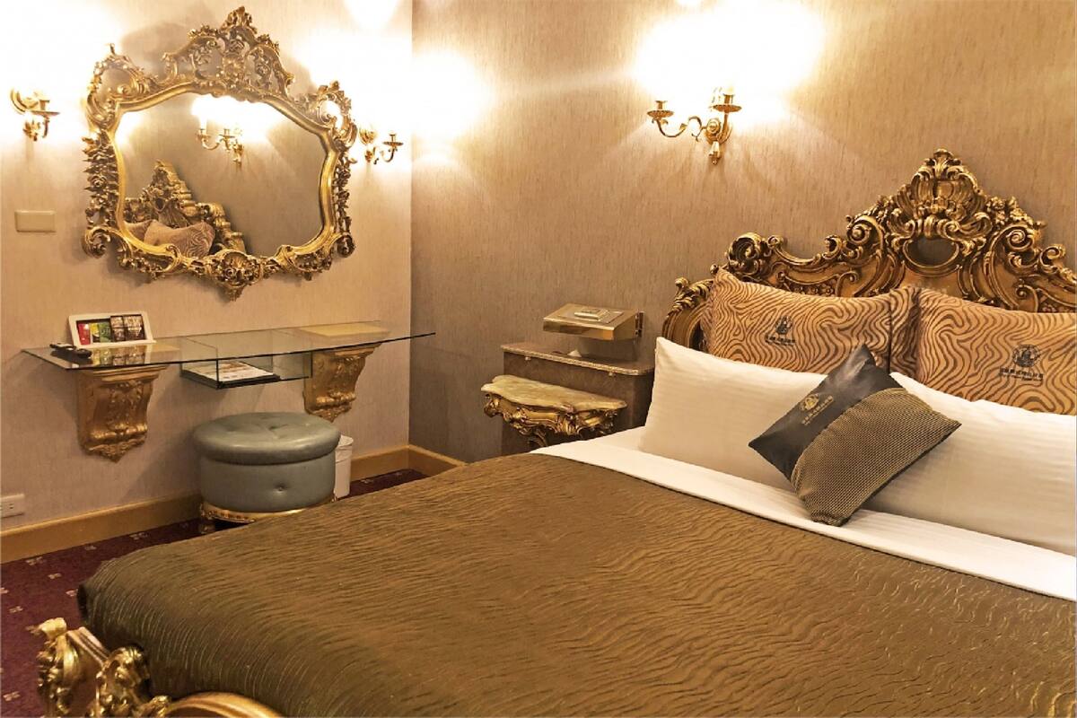 A room with a large bed, ornate headboard, a glass bedside table, and a mirror with an elaborate frame.