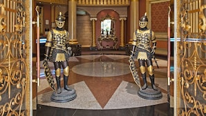 A grand lobby with ornate gold detailing, a mural on the ceiling, and two statues of armored figures. - The We Hotel (Taipei)