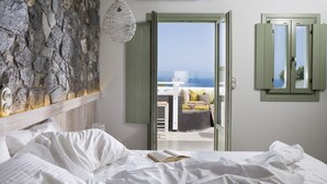 A bedroom with a bed, a view of the sea, and a stone wall. - Melograno Villas (Astypalaia)