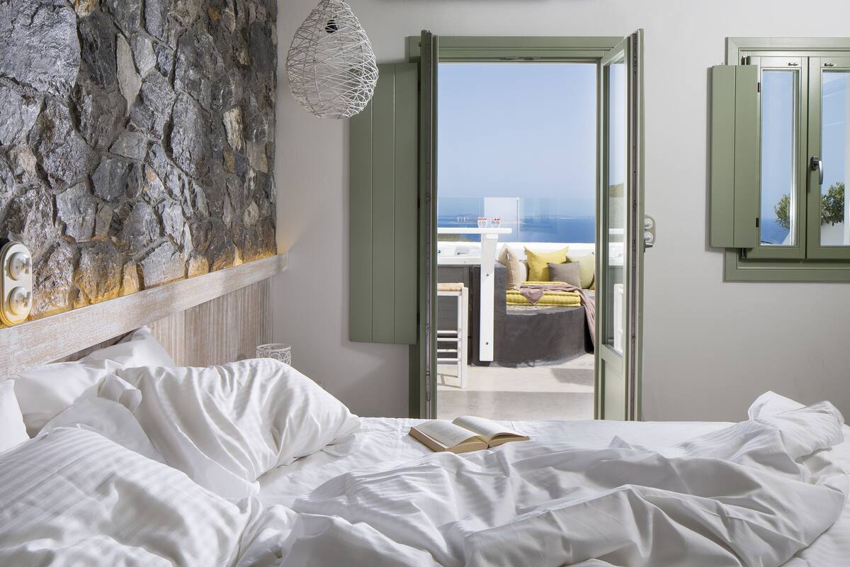 A bedroom with a bed, a view of the sea, and a stone wall.