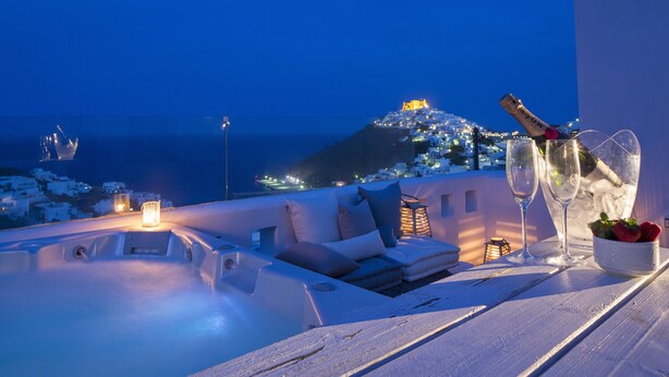 A rooftop terrace with a hot tub, lounge area, and a view of a hilltop cityscape at night. - Melograno Villas (Astypalaia)
