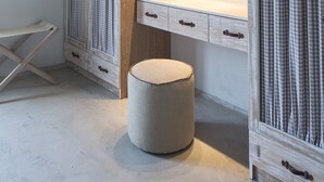 A compact bedroom with a wooden vanity, a round mirror, and a small round ottoman. - Melograno Villas (Astypalaia)