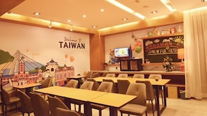 A hotel lobby with tables and chairs, a wall mural of Taiwan, a television, and a sign reading "Welcome to Taiwan".