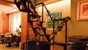 A hotel lobby with a staircase decorated with greenery, seating area with tables and chairs, and a printer on a desk.