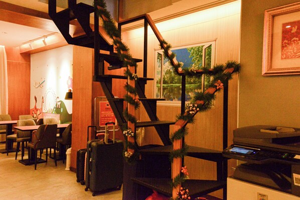 A hotel lobby with a staircase decorated with greenery, seating area with tables and chairs, and a printer on a desk. - Newful Hotel (Taipei)
