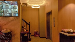 A hotel lobby with a marble floor, a wooden staircase, a chandelier, and a flat-screen TV displaying security cameras.