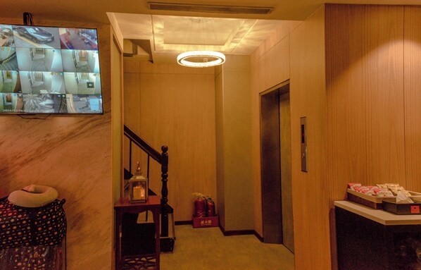 A hotel lobby with a marble floor, a wooden staircase, a chandelier, and a flat-screen TV displaying security cameras. - Newful Hotel (Taipei)