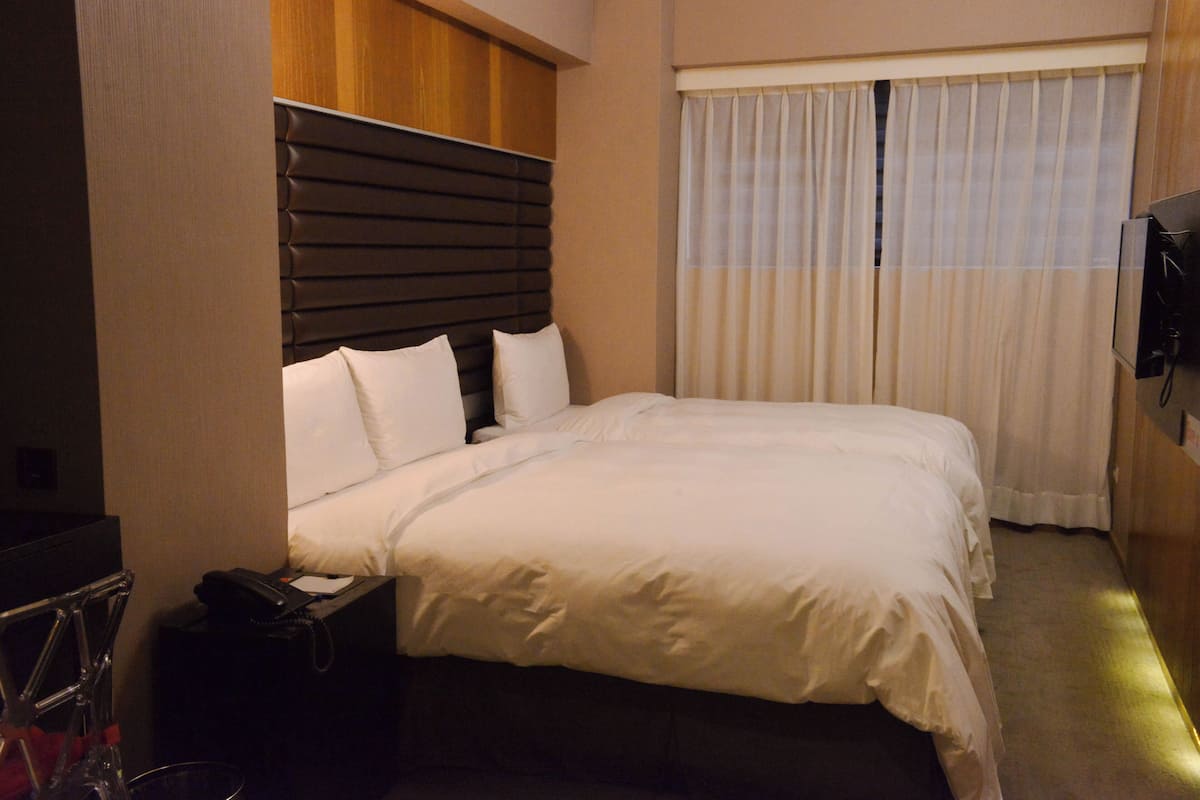 A hotel room with a large bed, a wooden headboard, a bedside table with a phone, and a TV mounted on the wall.