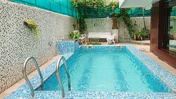 Relax by the pool surrounded by lush greenery and a vibrant mosaic wall.