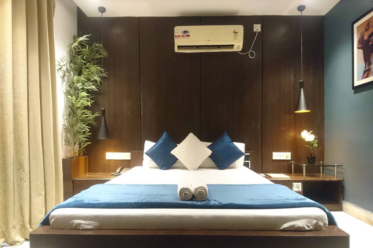 Habitación de hotel moderna con una cama grande, una planta en maceta, un escritorio con lámpara y un equipo de aire acondicionado en la pared.