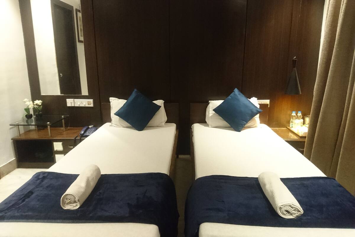 Habitación de hotel con dos camas, cada una con una manta y almohada azules, una mesita con un jarrón de flores y un espejo en la pared.