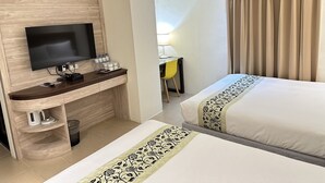 Ein Hotelzimmer mit Fernseher, Schreibtisch mit Lampe, zwei Betten mit dekorativen Tagesdecken und einem Vorhang.