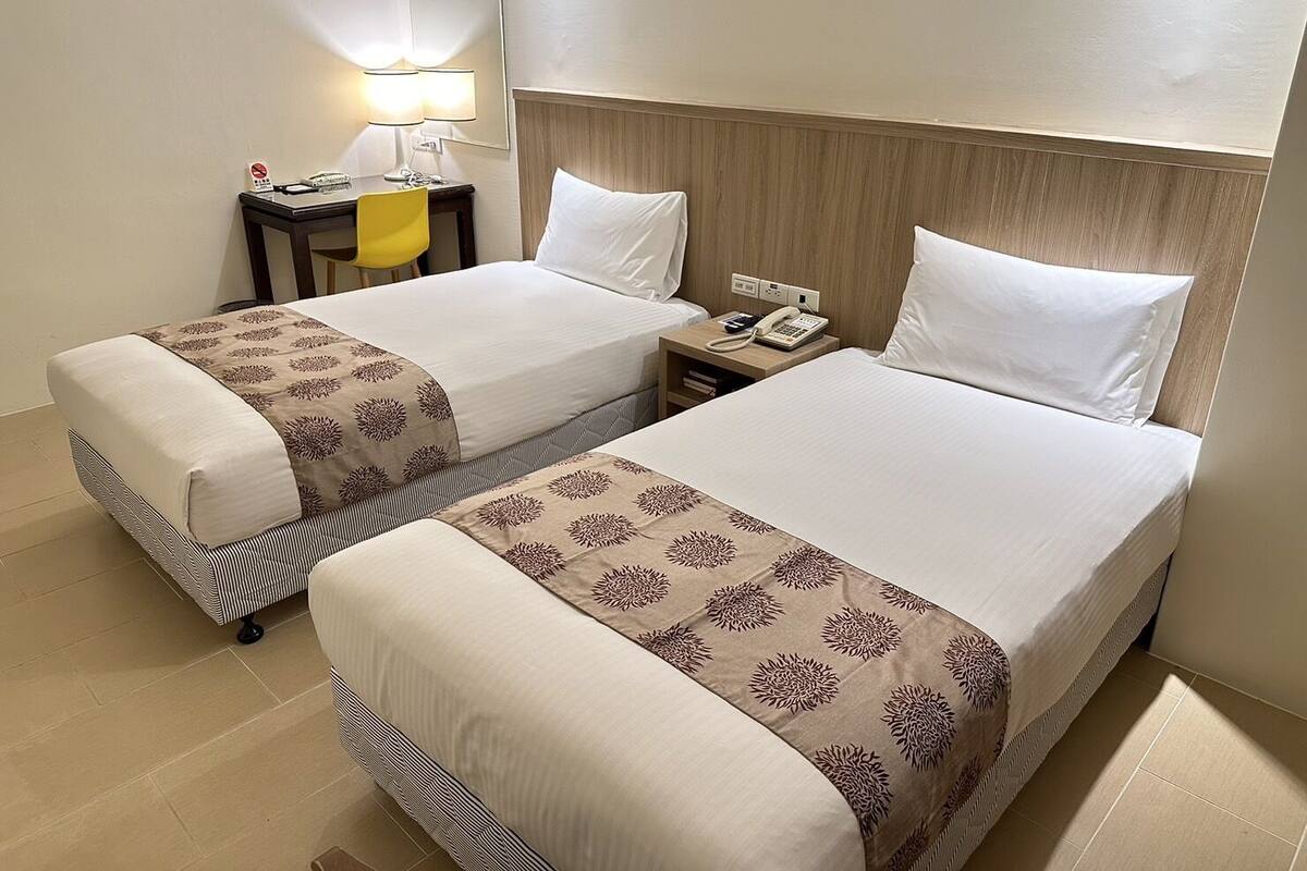 A hotel room with two beds, a desk with a lamp, and a telephone.