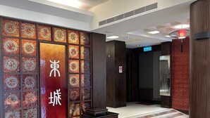 Ein Hotel-Lobbybereich mit einer Wandverzierung in chinesischen Schriftzeichen, einem Empfangstresen und einem roten Teppich.