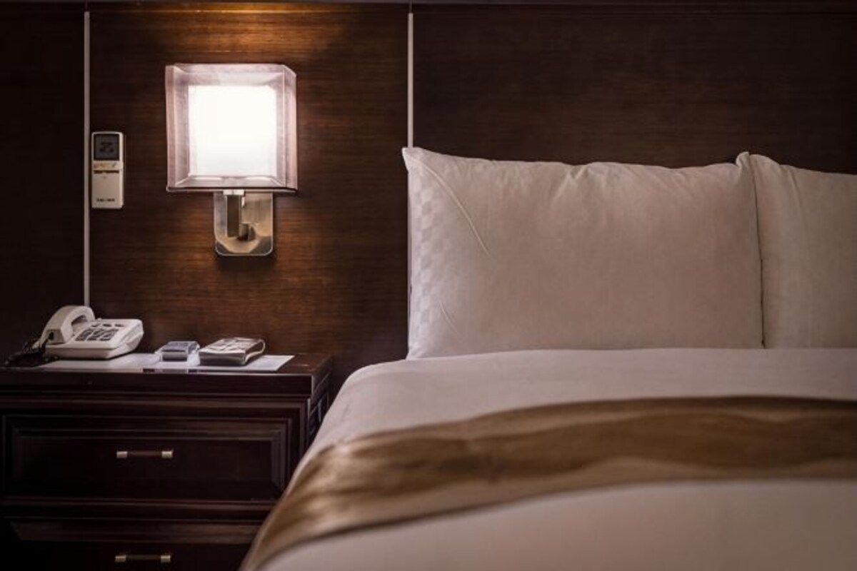 Ein Hotelzimmer mit einem Bett, einem Nachttisch mit Telefon und Lampe sowie einer Wandleuchte.