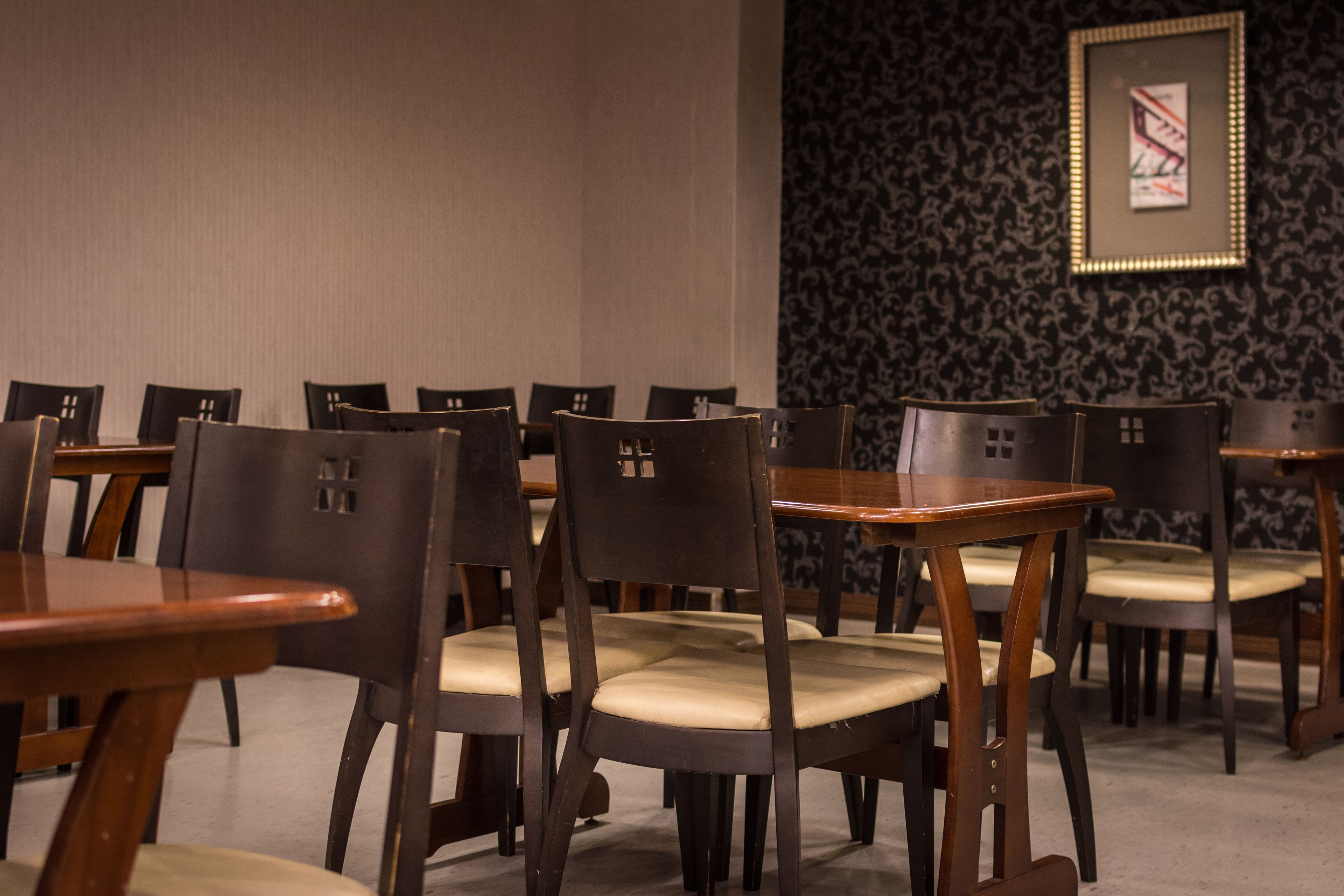 Un espace repas comprenant plusieurs tables et chaises, un mur orné de motifs et un tableau encadré.