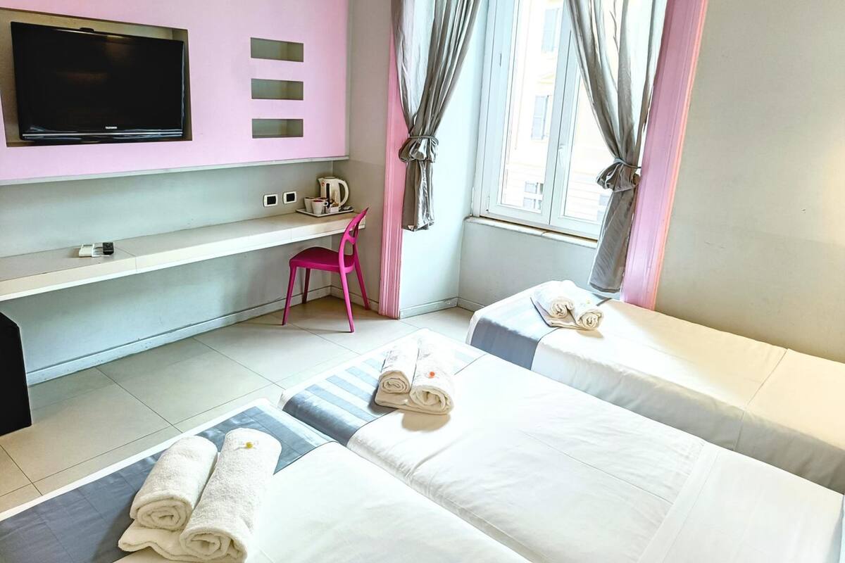 Une chambre d’hôtel avec deux lits, un bureau, une télévision et une fenêtre avec des rideaux.