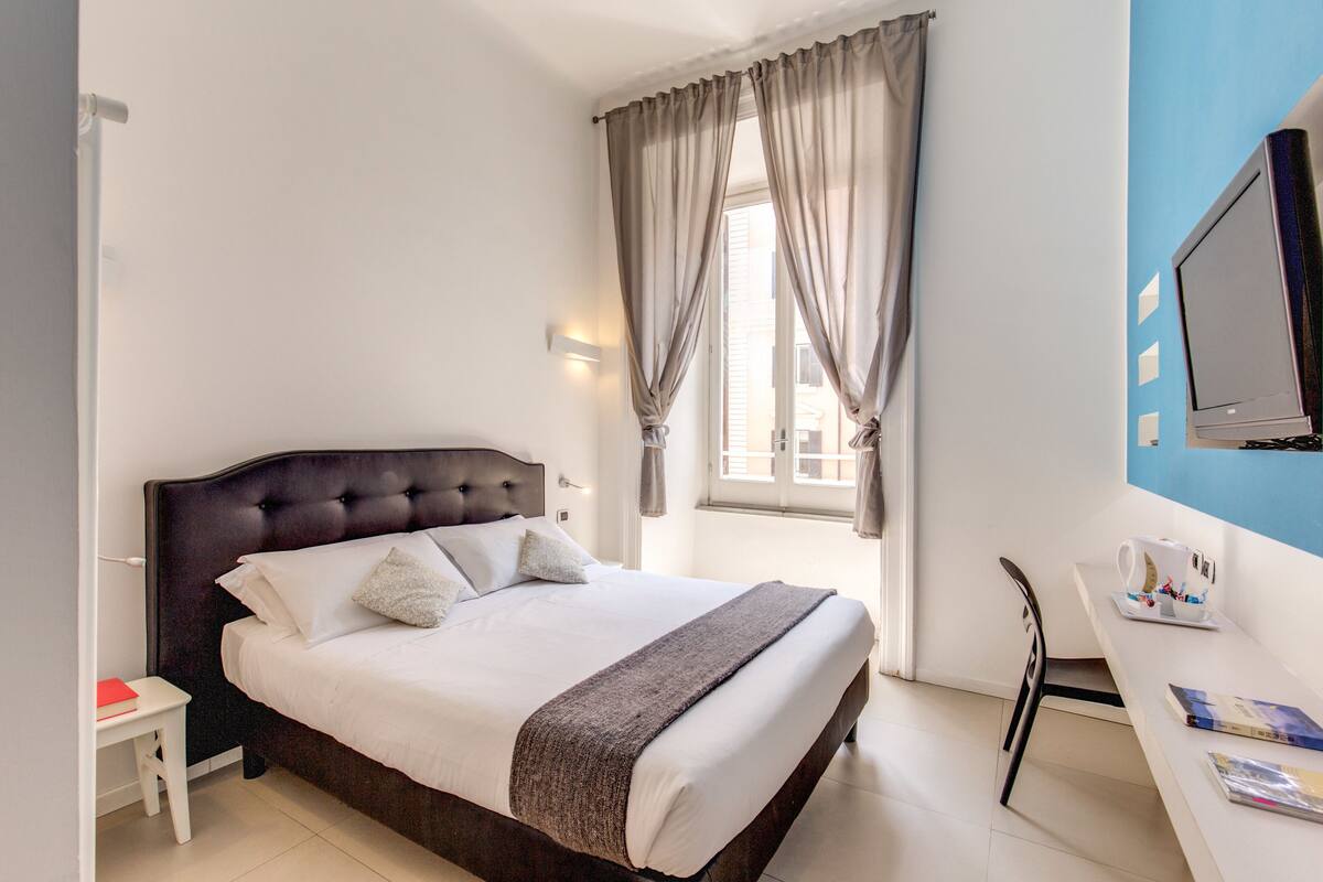 Une chambre à coucher avec un grand lit, une table de chevet, un bureau avec une chaise et un téléviseur fixé au mur.