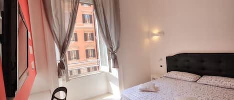 A bedroom with a bed, a chair, a TV, and a window with curtains.