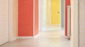 Un pasillo con una puerta blanca a la izquierda, una pared roja y una puerta amarilla al final.
