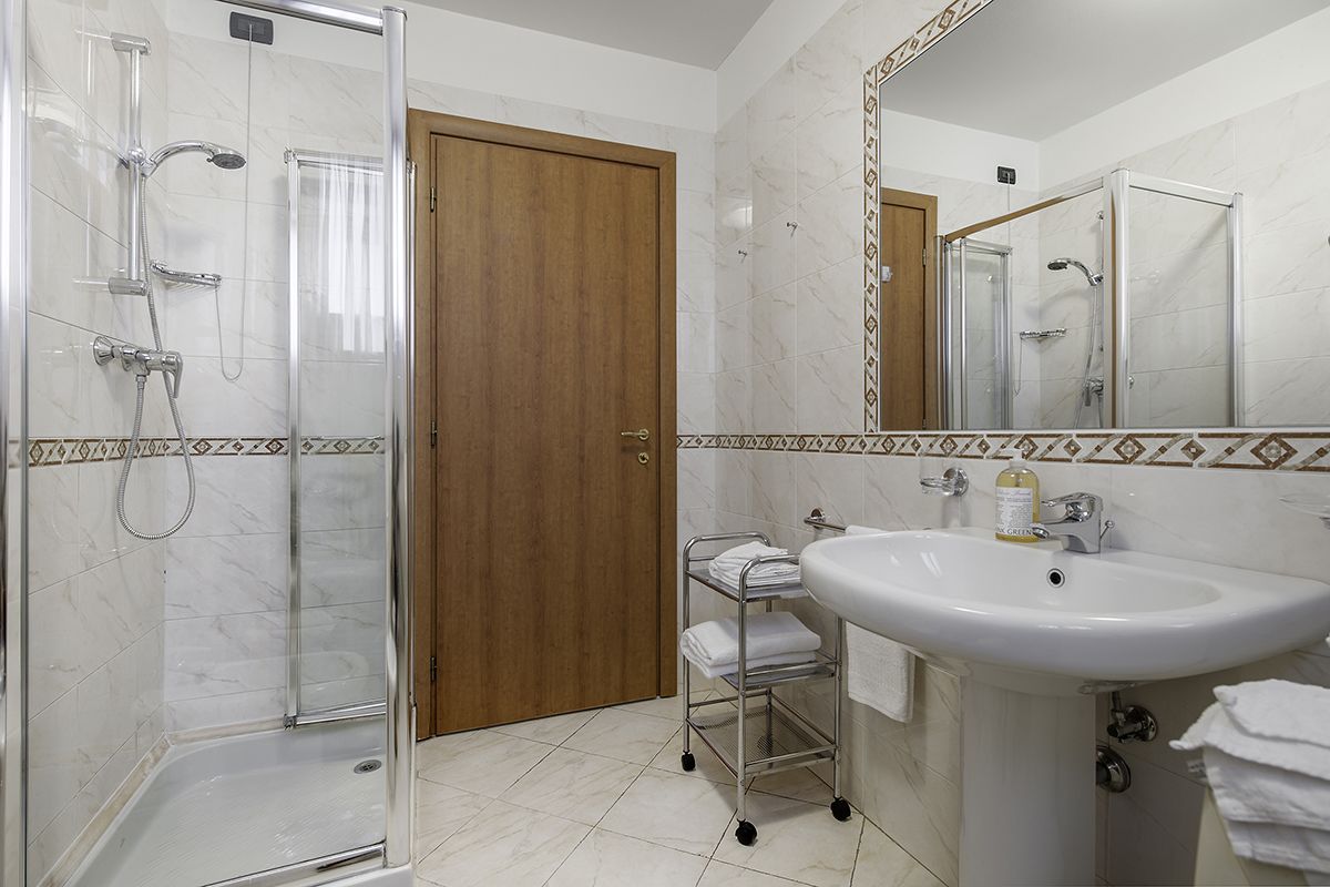 Une salle de bain avec une douche à parois de verre, une porte en bois, un lavabo avec un miroir et un sol carrelé.