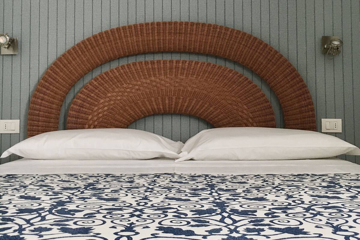 A bed with a patterned bedspread, a curved wooden headboard, and a plain wall with a switchboard.