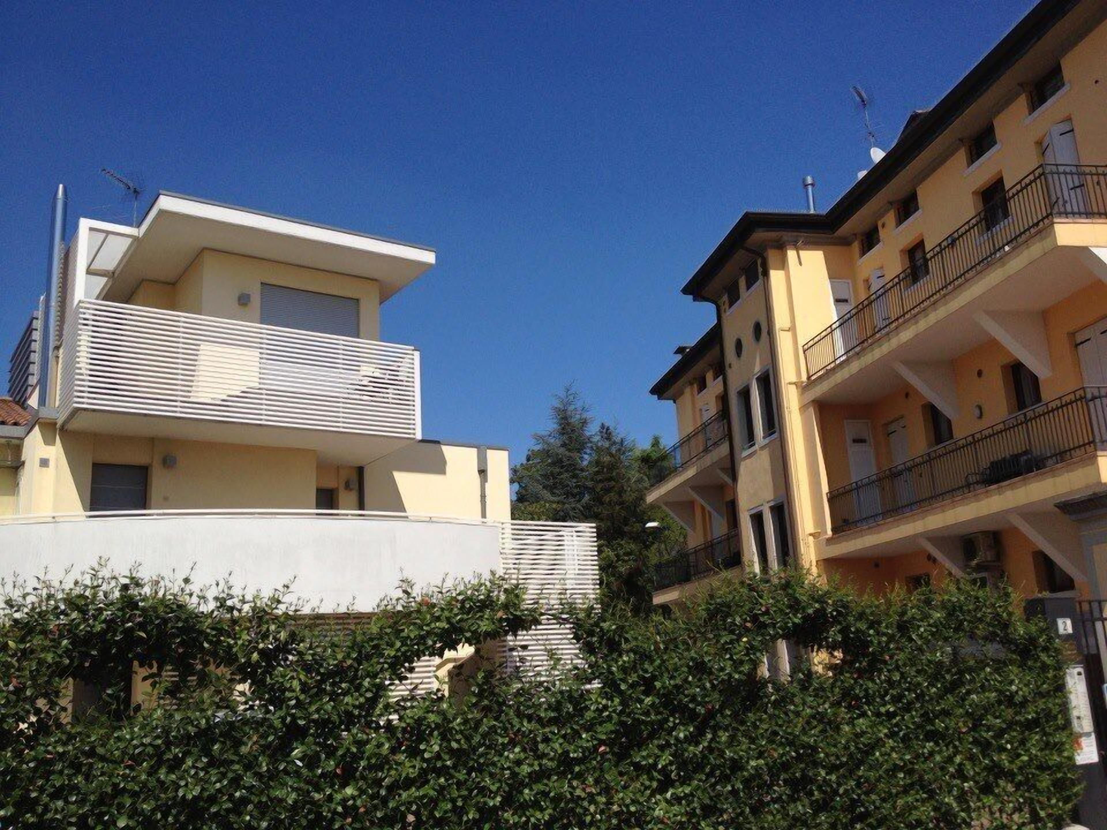A modern apartment building with a flat roof, balconies, and a clear blue sky.