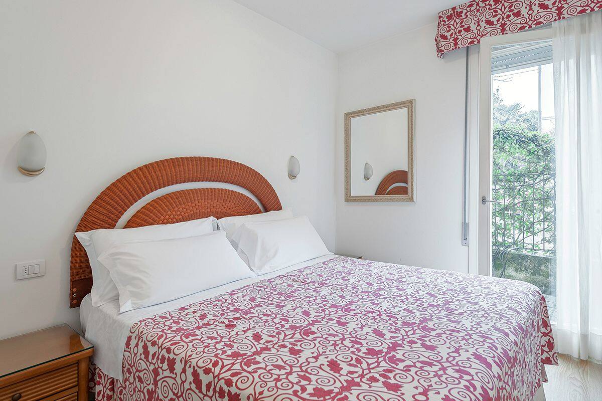 A bedroom with a bed, a nightstand, a mirror, and a window with curtains.