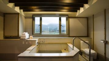 A modern bathroom with a large bathtub, a toilet, and a window offering a view of mountains.
