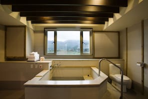 A modern bathroom with a large bathtub, a toilet, and a window offering a view of mountains.