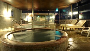 Zona de piscina interior climatizada con dos jacuzzis, sillones reclinables y suelo de baldosas.