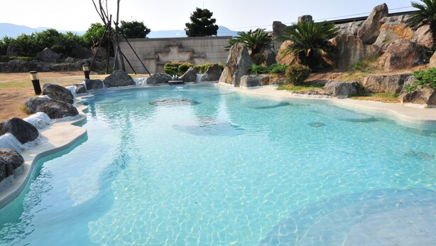 Una piscina cristalina con fondo de piedras, rodeada de rocas y un borde de hormigón.