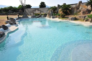 Una piscina cristalina con fondo de piedras, rodeada de rocas y un borde de hormigón.