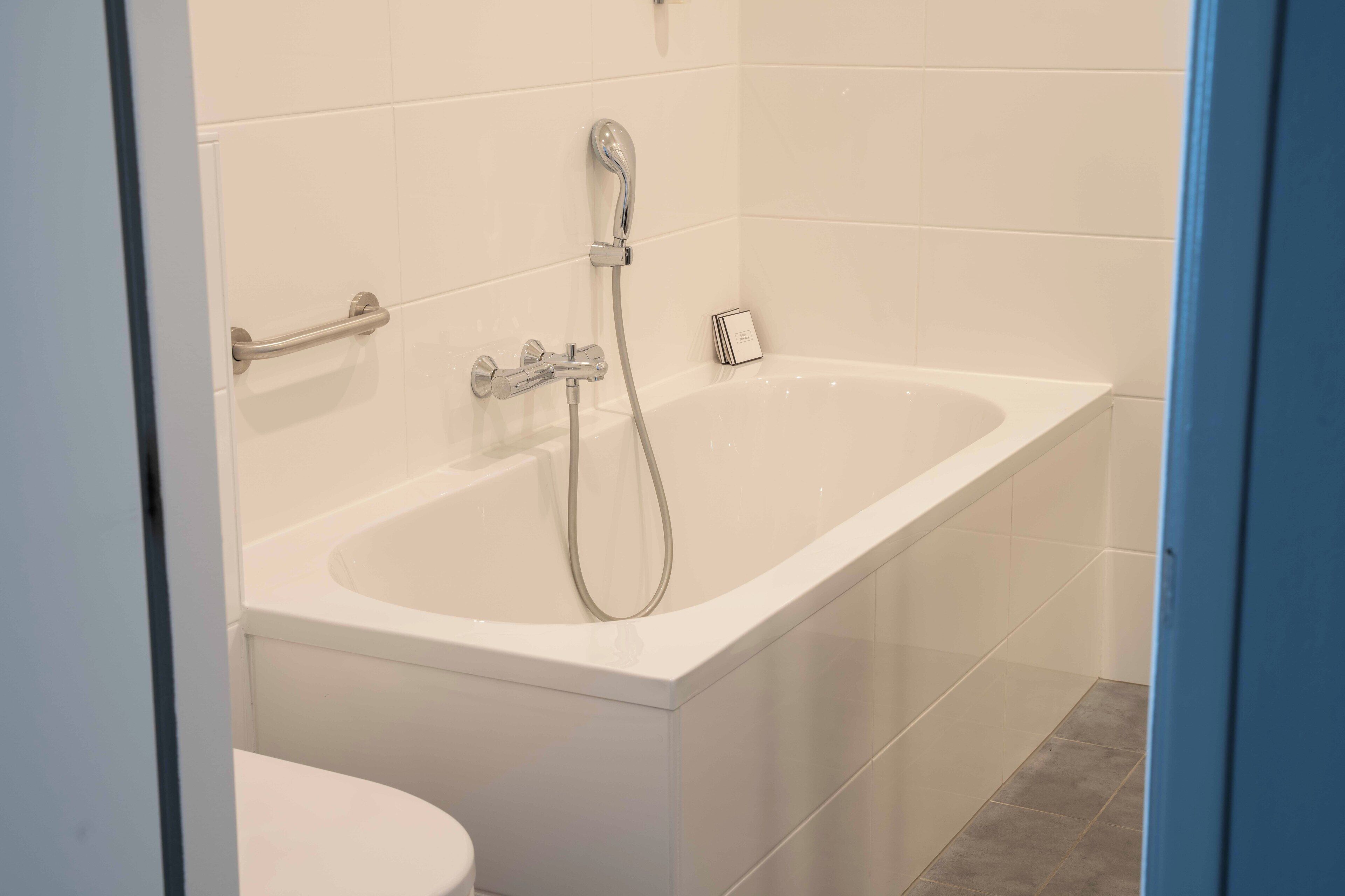 A modern bathroom with a white bathtub, a handheld showerhead, and a toilet.