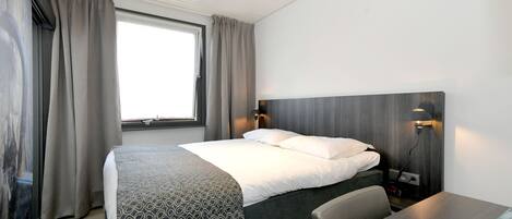 Une chambre d’hôtel moderne avec un lit bien fait, un bureau et une grande fenêtre avec des rideaux.