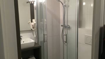Ett modernt badrum med en dusch som är avskärmad med glasväggar, ett vitt handfat och en handdukshängare.