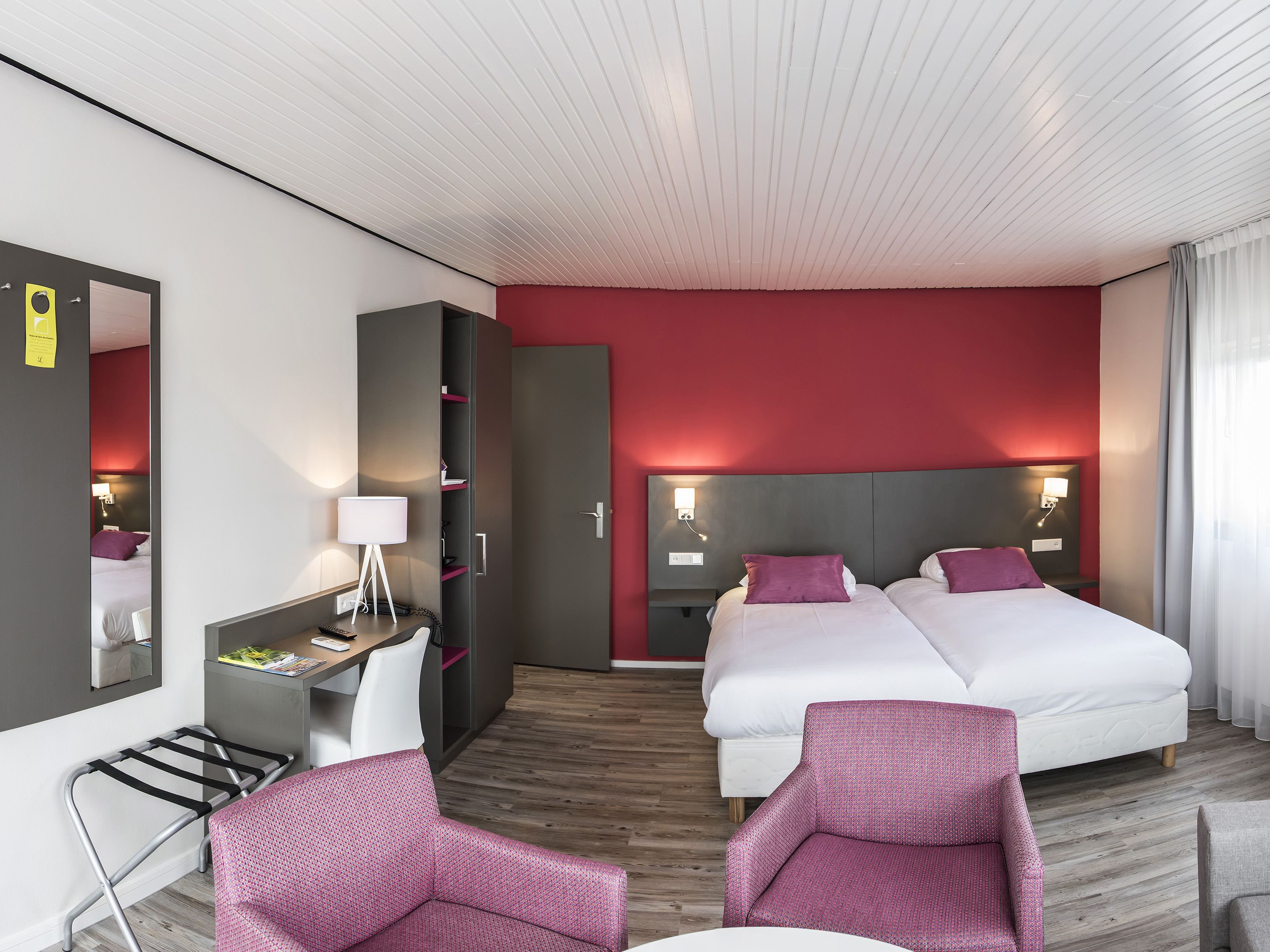 Et moderne hotelværelse med to senge, et skrivebord, en stol og et skab.
